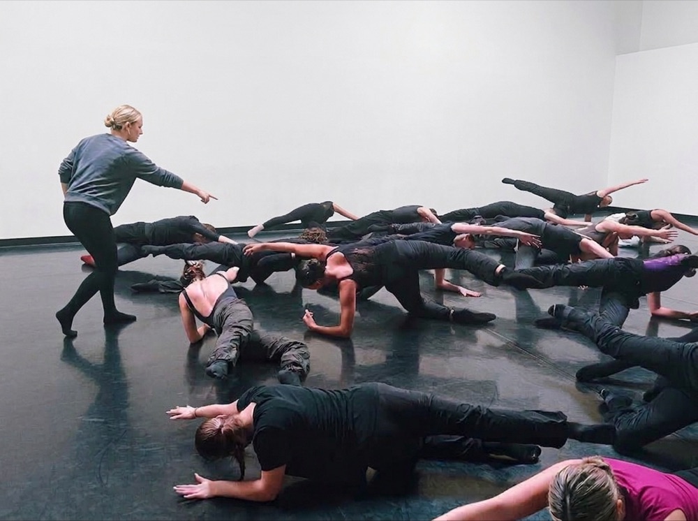 A teacher leading a group of dancers through a floor exercise in a studio.